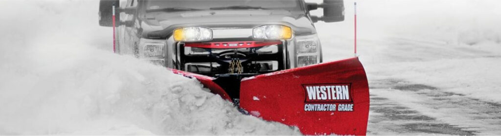 Wide view of a truck with a red contractor grade Western snow plow plowing snow on the street.